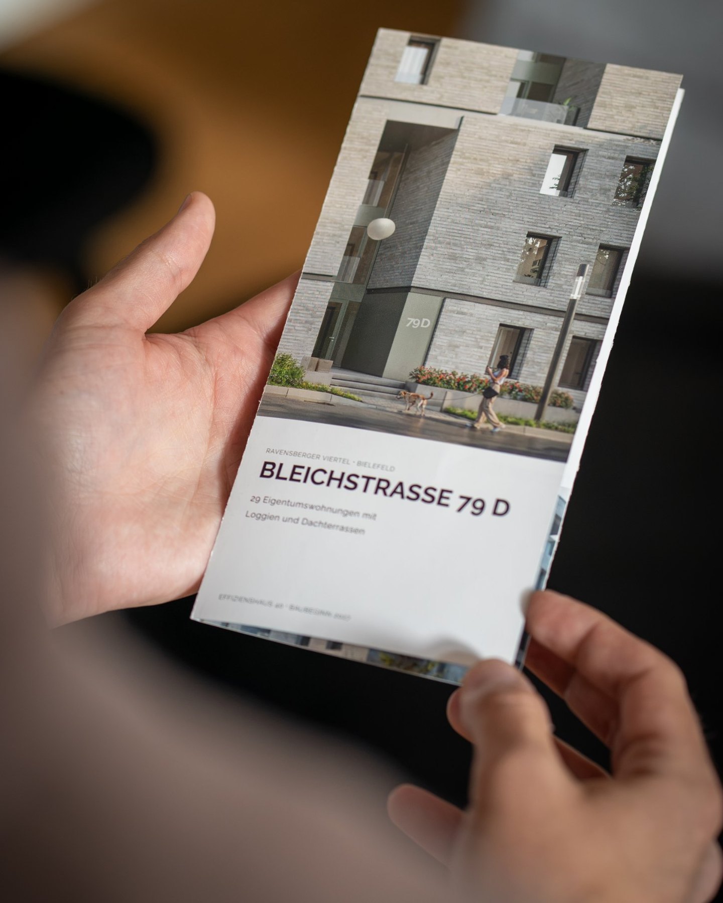 Hand hält das Trifold zur Bleichstraße 79 D, auf dem Titel der Hauseingang mit der Hausnummer 79 D